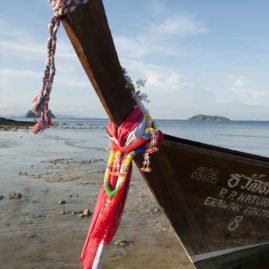 the prow of a traditional long tail boat moored on the beach at phi phi island phuket. Wrapped around the prow are multi coloured ribbons and silks in tribute to buddha, known as the Buddha Point