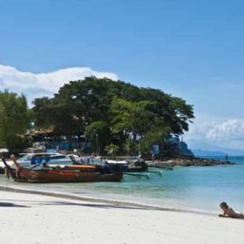 a row of thai long tail boats moored at a sandy beach on phi phi island zeavola hotel with a sexy girl lying in the surf free stock photo