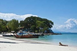 a row of thai long tail boats moored at a sandy beach on phi phi island zeavola hotel with a sexy girl lying in the surf free stock photo